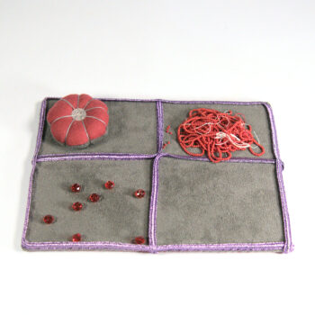 Pâté de broderie. Fond gris, soutache violette formant 4 cases. Des perles rouges facetées et un "pompon de perles rouges sont disposées dans les cases. Elles sont assorties au coussinet.