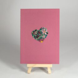 Carte rose brodée d'un coeur rempli de fleurs au ruban. Il y a aussi des perles vertes et jaunes. Une breloque abeille butine les fleurs.