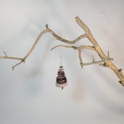 Branche sèche sur laquelle est accroché un sapin formé par des boutons mauves/violets empilés du plus grand en bas au plus petit en haut et surmonté d'une perle. De petites perles sont intercalées entre les boutons pour leur donner un peu de hauteur et un côté dansant. Une perles en bois suggère le tronc. Une ficelle dorée permet de le suspendre.