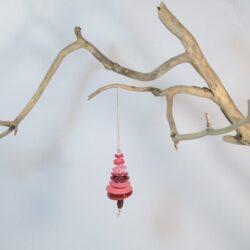 Branche sèche sur laquelle est accroché un sapin formé par des boutons roses empilés du plus grand en bas au plus petit en haut et surmonté d'une perle. De petites perles sont intercalées entre les boutons pour leur donner un peu de hauteur et un côté dansant. Une perles en bois suggère le tronc. Une ficelle dorée permet de le suspendre.