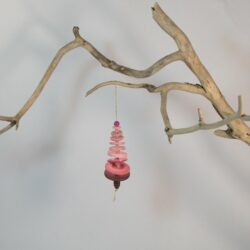 Branche sèche sur laquelle est accroché un sapin formé par des boutons roses empilés du plus grand en bas au plus petit en haut et surmonté d'une perle. De petites perles sont intercalées entre les boutons pour leur donner un peu de hauteur et un côté dansant. Une perles en bois suggère le tronc. Une ficelle dorée permet de le suspendre.