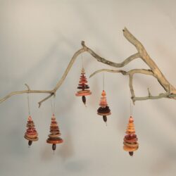 Branche sèche sur laquelle sont suspendus des sapins formés par des boutons orangés empilés du plus grand en bas au plus petit en haut et surmonté d'une perle. De petites perles sont intercalées entre les boutons pour leur donner un peu de hauteur et un côté dansant. Des perles en bois suggèrent les troncs. Une ficelle dorée permet de les suspendre.